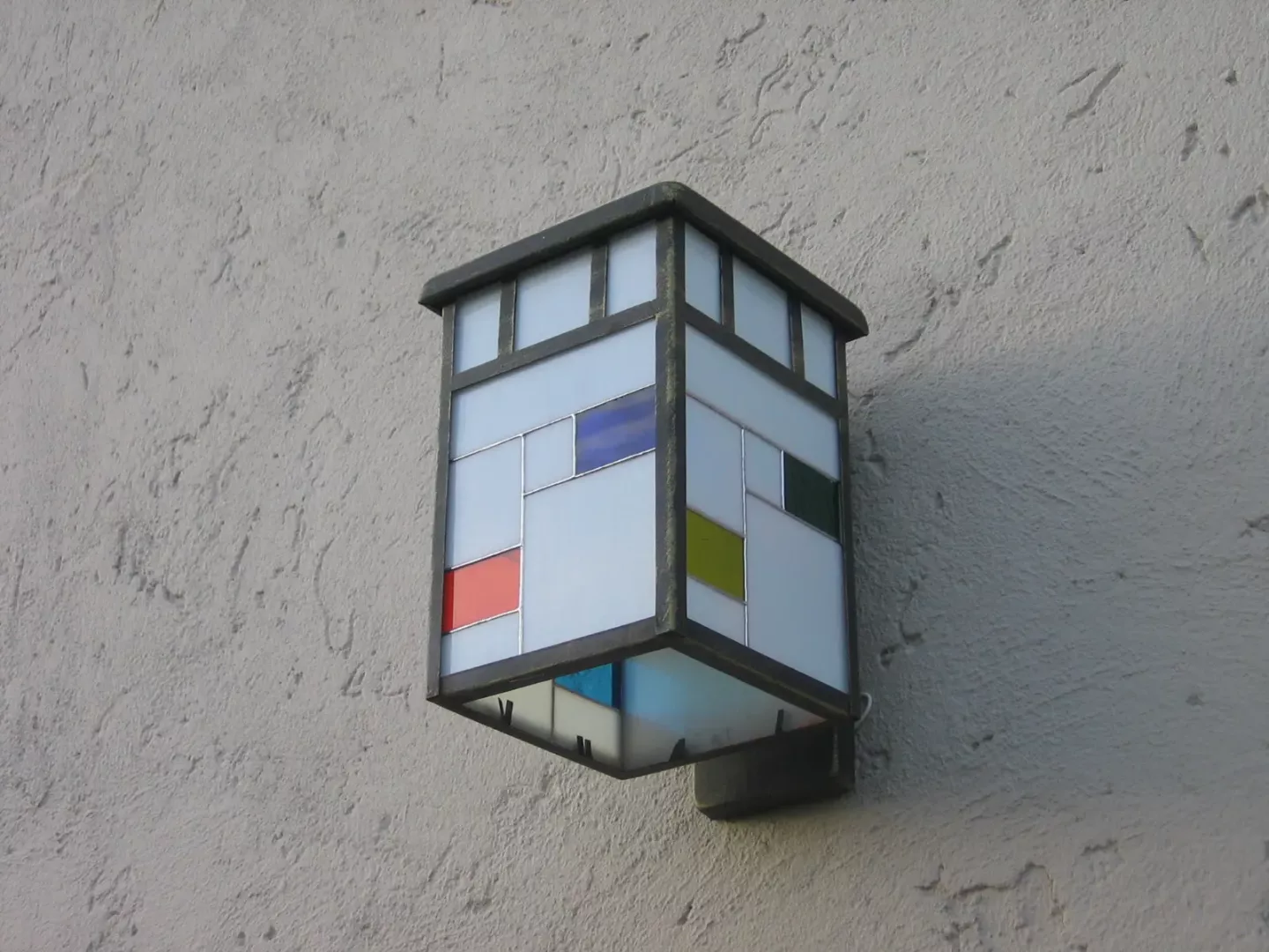 Farol de pared con vidrios blancos y pequeños paneles de color.