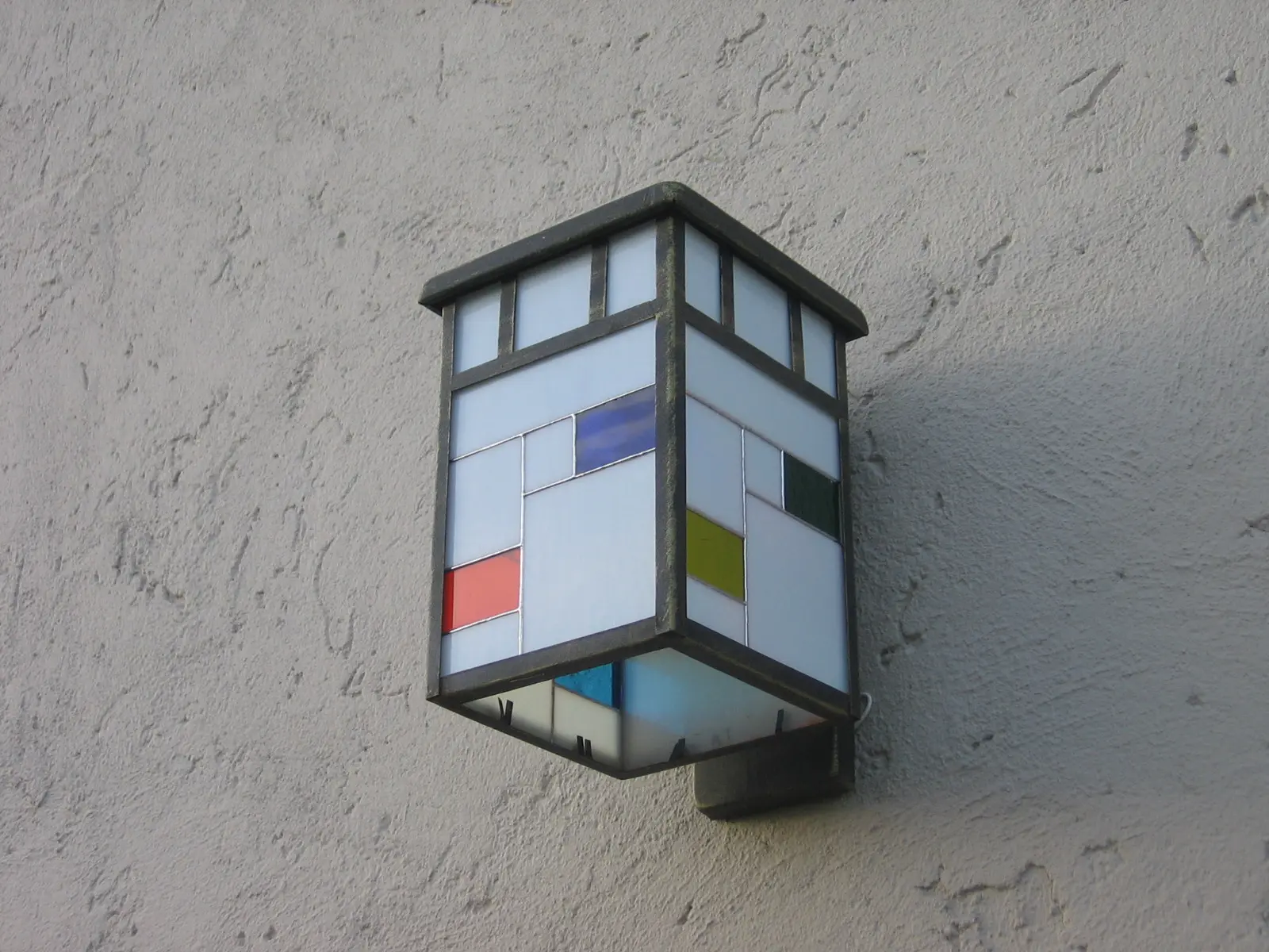 Farol de pared con vidrios blancos y pequeños paneles de color.