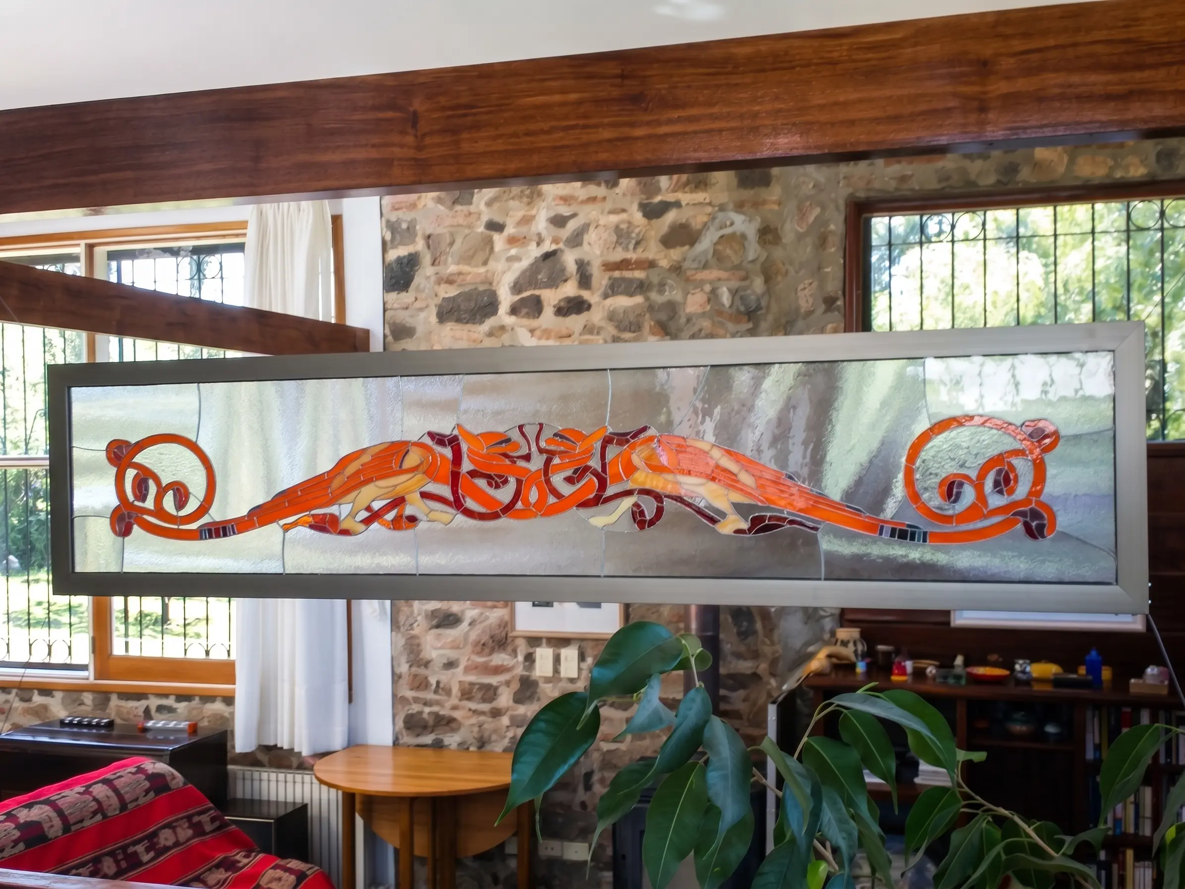 Vitral horizontal con un dragón rojo y naranja, instalado en un ambiente con madera y piedra.